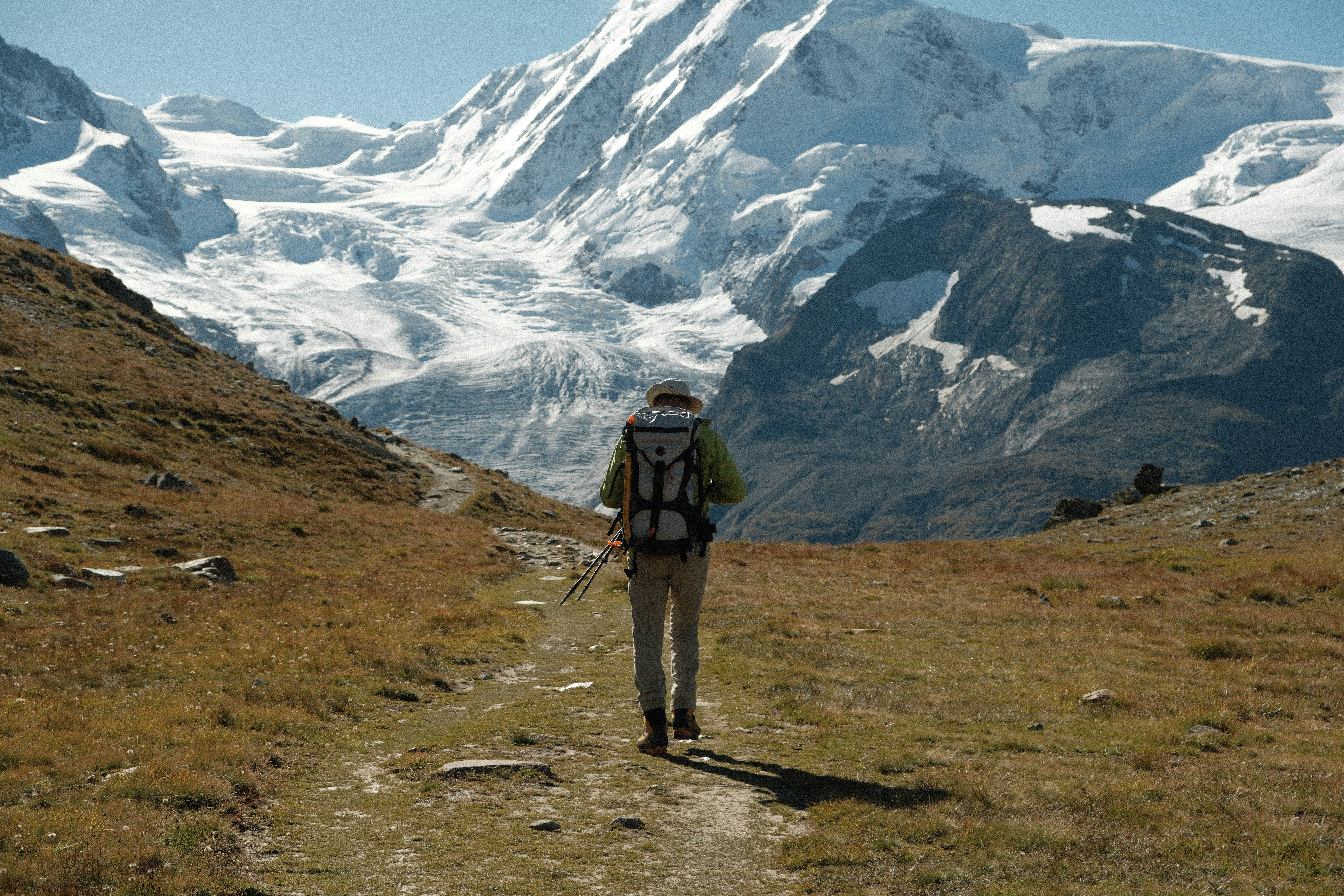 A man with a backpack is hiking up a hill