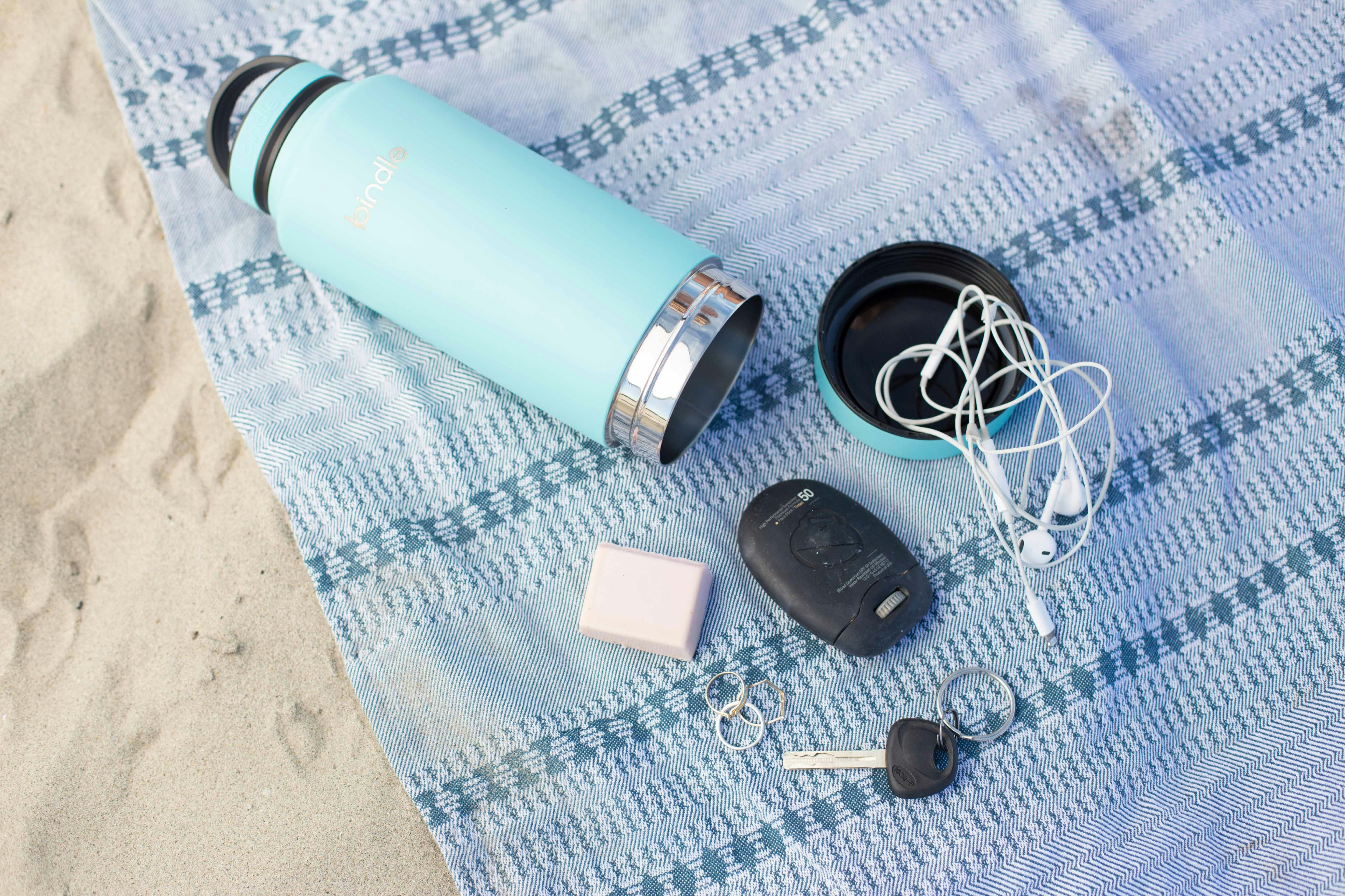 teal stainless steel travel mug with fob, key and earbuds on blue textile